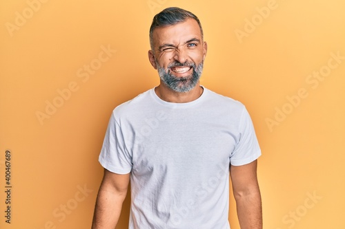 Middle age handsome man wearing casual white tshirt winking looking at the camera with sexy expression, cheerful and happy face.