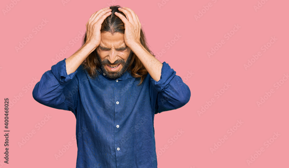 Attractive man with long hair and beard wearing casual clothes suffering from headache desperate and stressed because pain and migraine. hands on head. Attractive man with long hair and beard wearing casual clothes suffering from headache desperate and stressed because pain and migraine. hands on head.