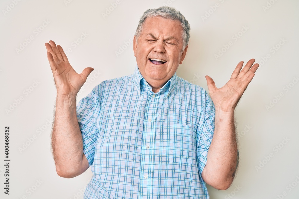 Naklejka premium Senior grey-haired man wearing casual clothes celebrating mad and crazy for success with arms raised and closed eyes screaming excited. winner concept