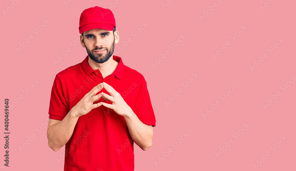 Young handsome man with beard wearing delivery uniform hands together and fingers crossed smiling relaxed and cheerful. success and optimistic Young handsome man with beard wearing delivery uniform hands together and fingers crossed smiling relaxed and cheerful. success and optimistic