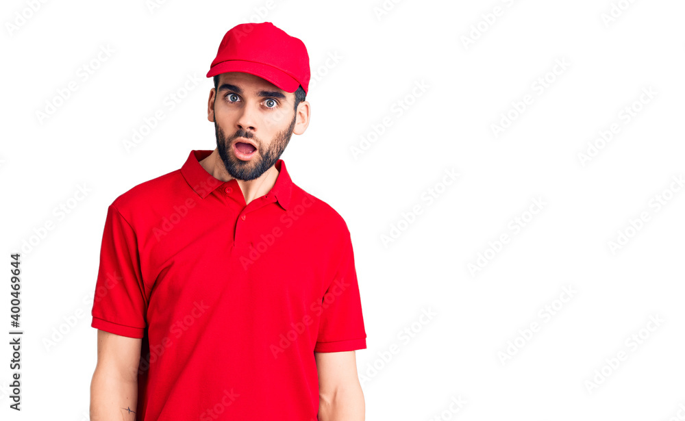 Young handsome man with beard wearing delivery uniform in shock face, looking skeptical and sarcastic, surprised with open mouth Young handsome man with beard wearing delivery uniform in shock face, looking skeptical and sarcastic, surprised with open mouth