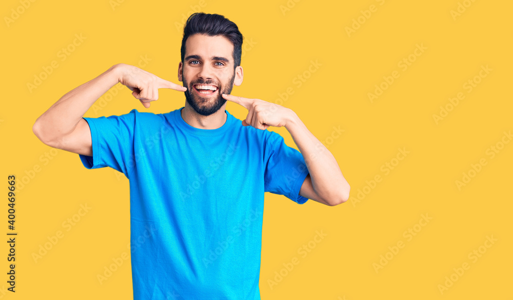 Young handsome man with beard wearing casual t-shirt smiling cheerful showing and pointing with fingers teeth and mouth. dental health concept. Young handsome man with beard wearing casual t-shirt smiling cheerful showing and pointing with fingers teeth and mouth. dental health concept.