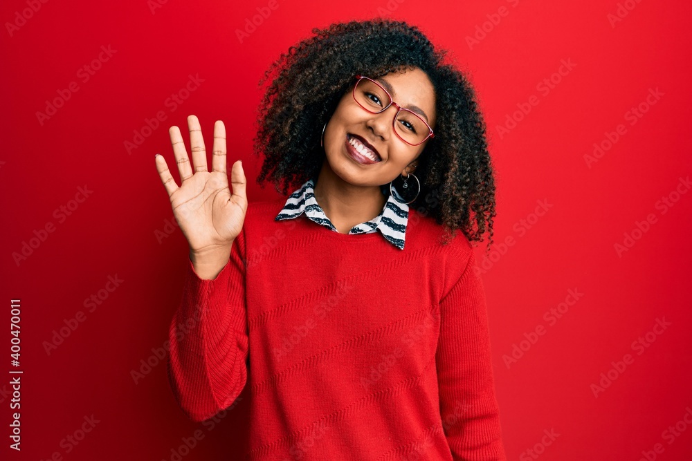Beautiful african american woman with afro hair wearing sweater and glasses waiving saying hello happy and smiling, friendly welcome gesture Beautiful african american woman with afro hair wearing sweater and glasses waiving saying hello happy and smiling, friendly welcome gesture