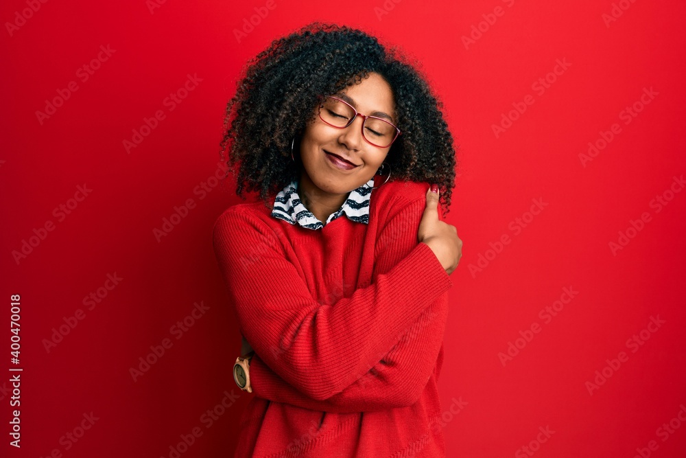 Beautiful african american woman with afro hair wearing sweater and glasses hugging oneself happy and positive, smiling confident. self love and self care Beautiful african american woman with afro hair wearing sweater and glasses hugging oneself happy and positive, smiling confident. self love and self care
