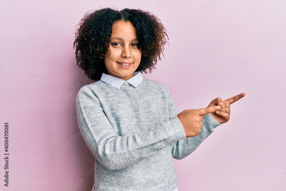 Young little girl with afro hair wearing casual clothes smiling and looking at the camera pointing with two hands and fingers to the side. Young little girl with afro hair wearing casual clothes smiling and looking at the camera pointing with two hands and fingers to the side.