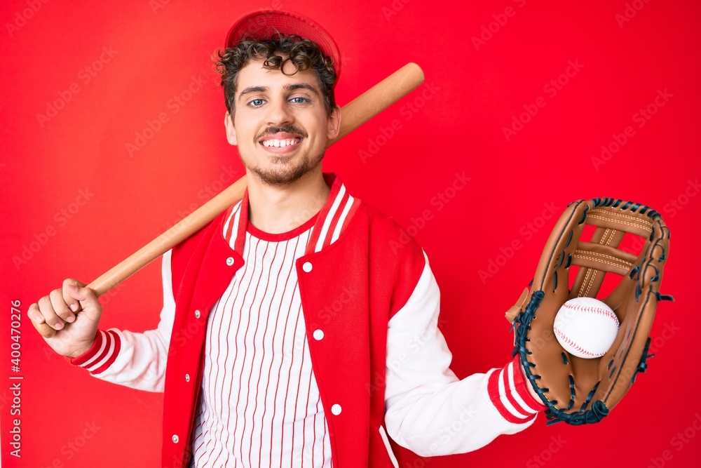 Young caucasian man with curly hair wearing baseball uniform holding ...