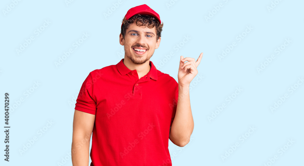 Young handsome man with curly hair wearing delivery uniform smiling happy pointing with hand and finger to the side Young handsome man with curly hair wearing delivery uniform smiling happy pointing with hand and finger to the side