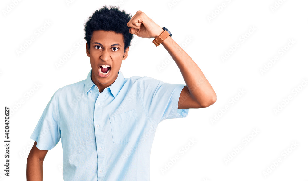 Young african american man wearing casual clothes angry and mad raising fist frustrated and furious while shouting with anger. rage and aggressive concept. Young african american man wearing casual clothes angry and mad raising fist frustrated and furious while shouting with anger. rage and aggressive concept.