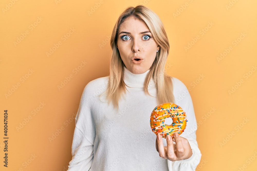 Young caucasian woman holding donut scared and amazed with open mouth for surprise, disbelief face Young caucasian woman holding donut scared and amazed with open mouth for surprise, disbelief face