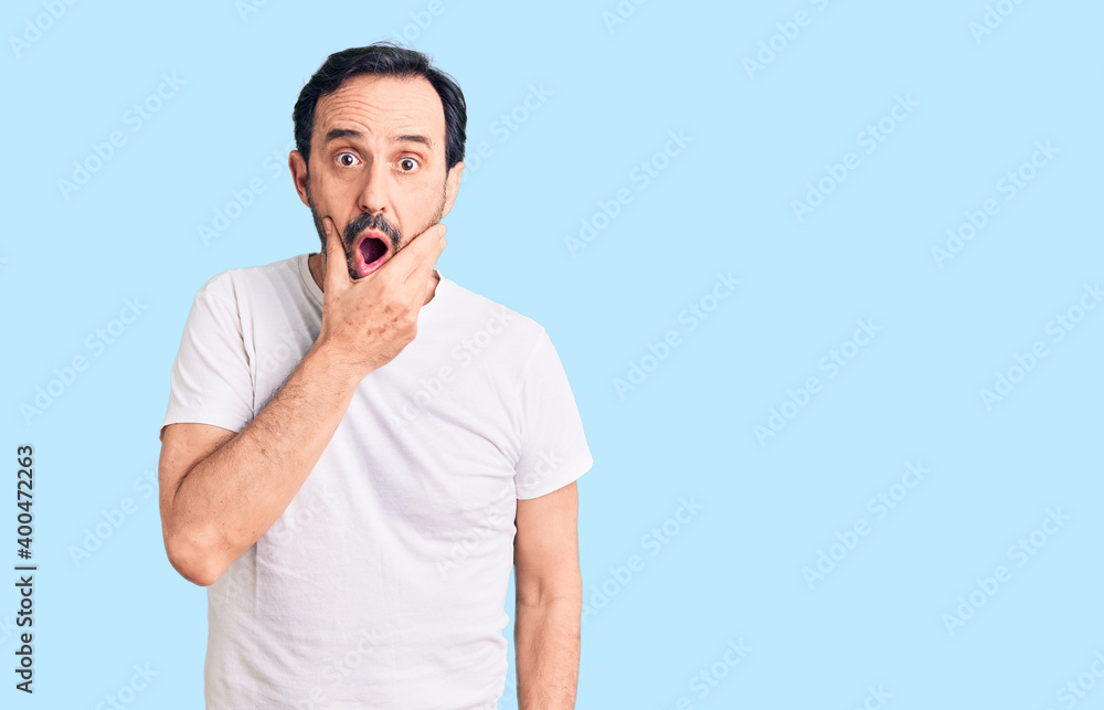 Middle age handsome man wearing casual t-shirt looking fascinated with disbelief, surprise and amazed expression with hands on chin Middle age handsome man wearing casual t-shirt looking fascinated with disbelief, surprise and amazed expression with hands on chin