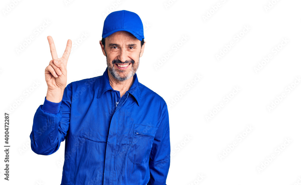 Middle age handsome man wearing mechanic uniform smiling looking to the camera showing fingers doing victory sign. number two.