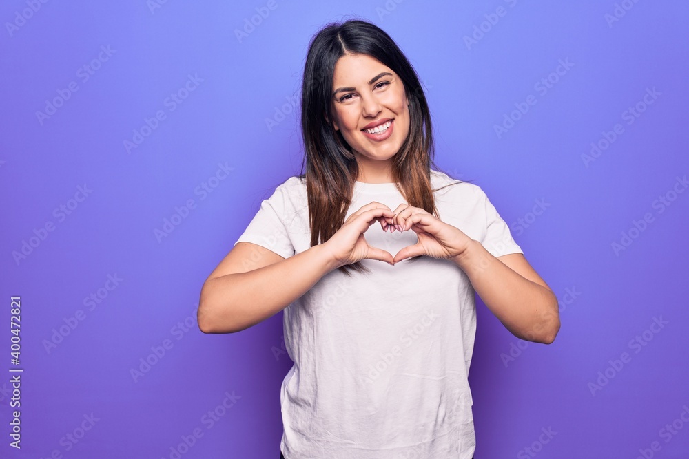 Young beautiful brunette woman wearing casual t-shirt standing over purple background smiling in love doing heart symbol shape with hands. Romantic concept. Young beautiful brunette woman wearing casual t-shirt standing over purple background smiling in love doing heart symbol shape with hands. Romantic concept.