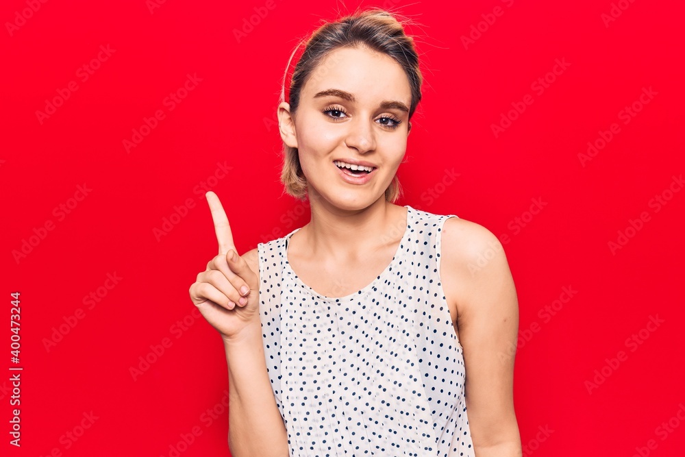 Young beautiful blonde woman wearing casual clothes smiling with an idea or question pointing finger up with happy face, number one Young beautiful blonde woman wearing casual clothes smiling with an idea or question pointing finger up with happy face, number one
