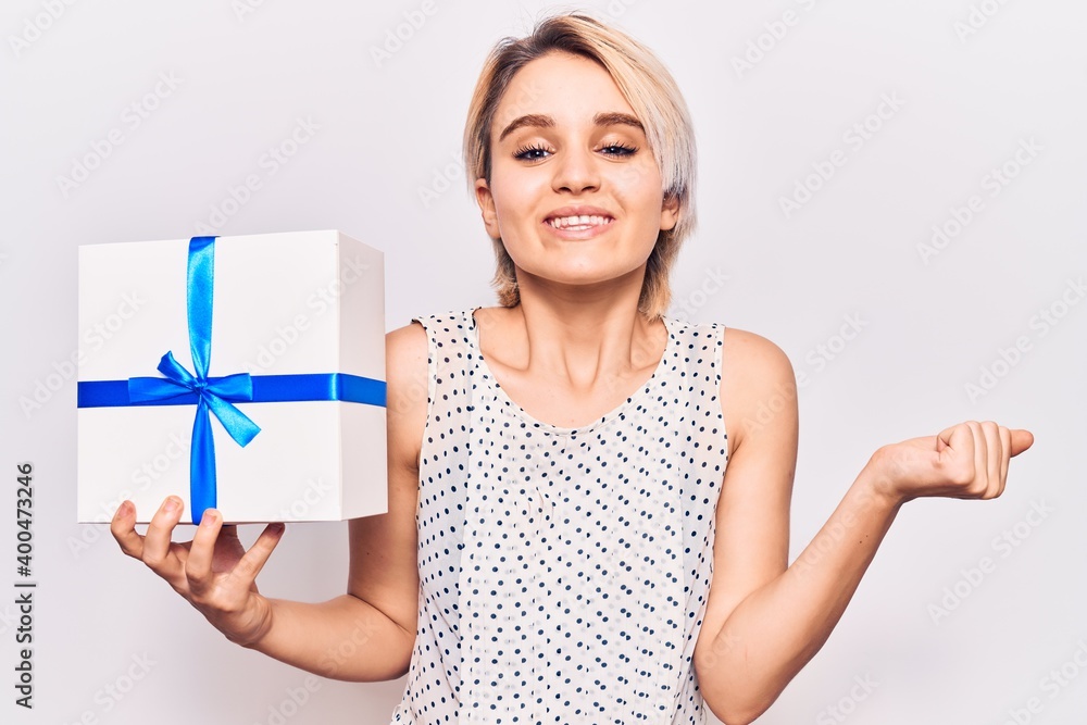Young beautiful blonde woman holding gift screaming proud, celebrating victory and success very excited with raised arm Young beautiful blonde woman holding gift screaming proud, celebrating victory and success very excited with raised arm