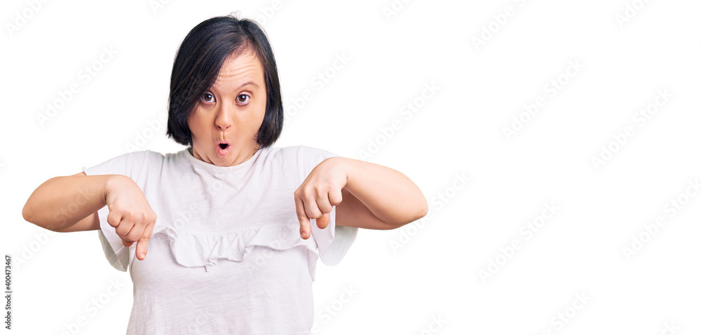 Brunette woman with down syndrome wearing casual white tshirt pointing down with fingers showing advertisement, surprised face and open mouth Brunette woman with down syndrome wearing casual white tshirt pointing down with fingers showing advertisement, surprised face and open mouth