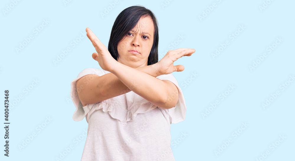 Brunette woman with down syndrome wearing casual white tshirt rejection expression crossing arms doing negative sign, angry face Brunette woman with down syndrome wearing casual white tshirt rejection expression crossing arms doing negative sign, angry face