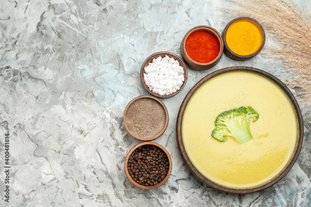 Creamy broccoli soup in a brown bowl and different spices on gray background Creamy broccoli soup in a brown bowl and different spices on gray background
