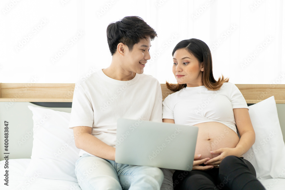 Happy Asian husband and wife living together in bedroom and browsing the internet for online shopping