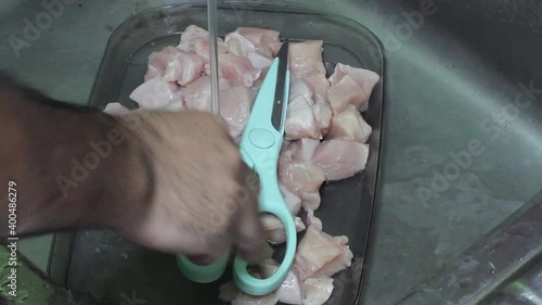 High angle view cutting chicken breast into pieces with a sharp meat scissor.