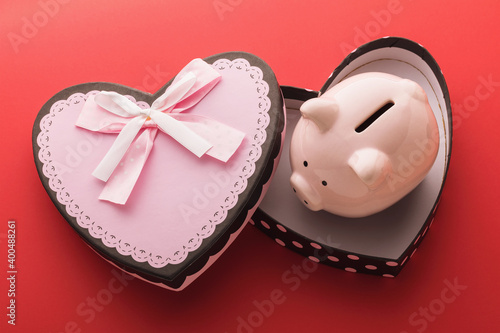 Piggy bank in an empty gift box on a red background. Concept on the topic of saving money for the holidays © Sergey Chayko