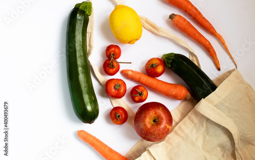 Flat lay of a reusable bag with organic groceries on a white background. Apples, zucchini, carrots, lemon and tomatoes