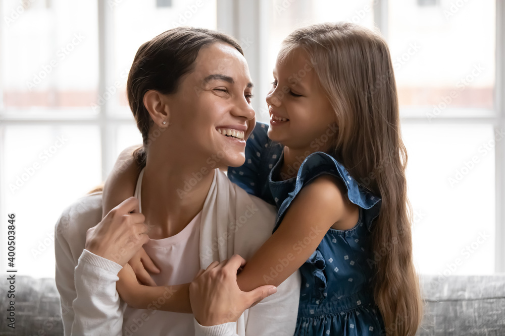 Close up smiling little girl hugging young beautiful mother, enjoying tender moment, happy mum and adorable daughter embracing, having fun together, sitting on cozy couch at home, good relationship Close up smiling little girl hugging young beautiful mother, enjoying tender moment, happy mum and adorable daughter embracing, having fun together, sitting on cozy couch at home, good relationship