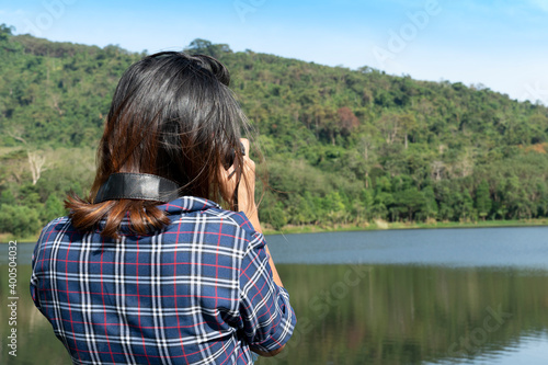 woman standing back to take a picture at a reservoir with green mountains in the background. Ang Kep Nam Huai Hin Dat Rayong Thailand.