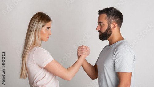 Young guy and girl look at each other seriously and squeeze their hands in arm wrestling