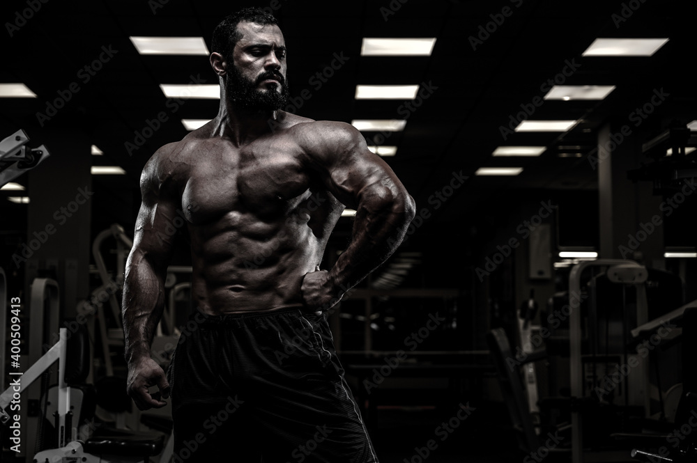 mighty strong athlete bearded male with sport physique body in dark fitness gym with copy space