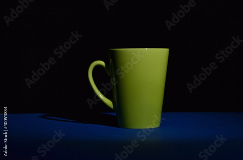 green ceramic cup in the darkness on blue desk and isolated on black background, copy space
