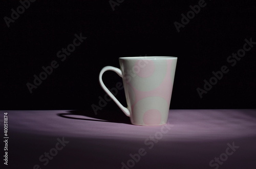 pink ceramic cup in the darkness on pink desk and isolated on black background, copy space