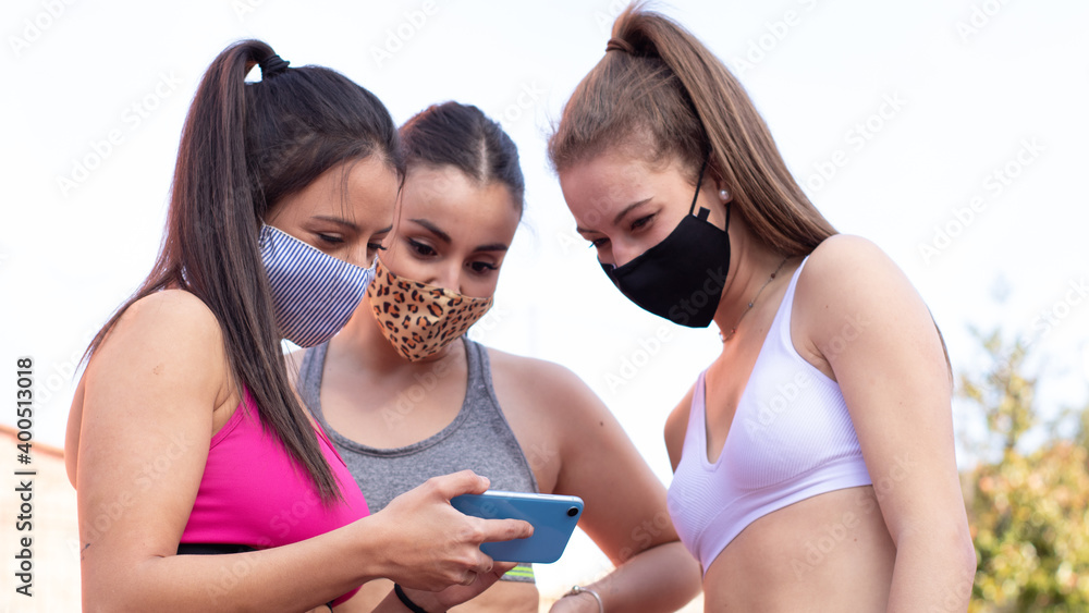 Three cheerful girls wearing masks look at a picture of a mobile phone while practicing basketball on a court in the city Three cheerful girls wearing masks look at a picture of a mobile phone while practicing basketball on a court in the city