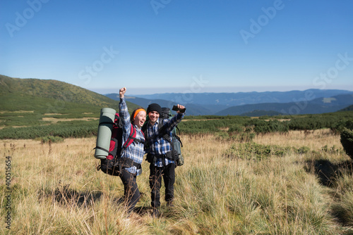 a couple of tourists in love, a man and a woman stand on a mountain plain raise their hands up and shout cheerfully. Hiking concept.