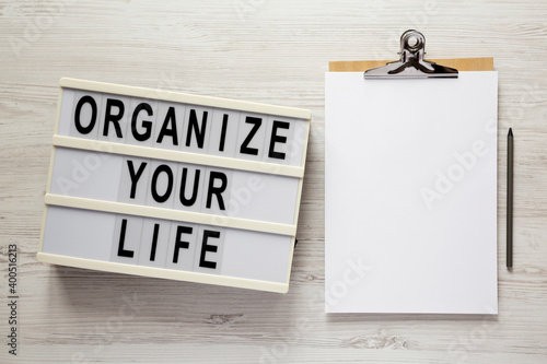 'Organize your life' on a lightbox, clipboard with blank sheet of paper on a white wooden surface, top view. Flat lay, overhead, from above. photo