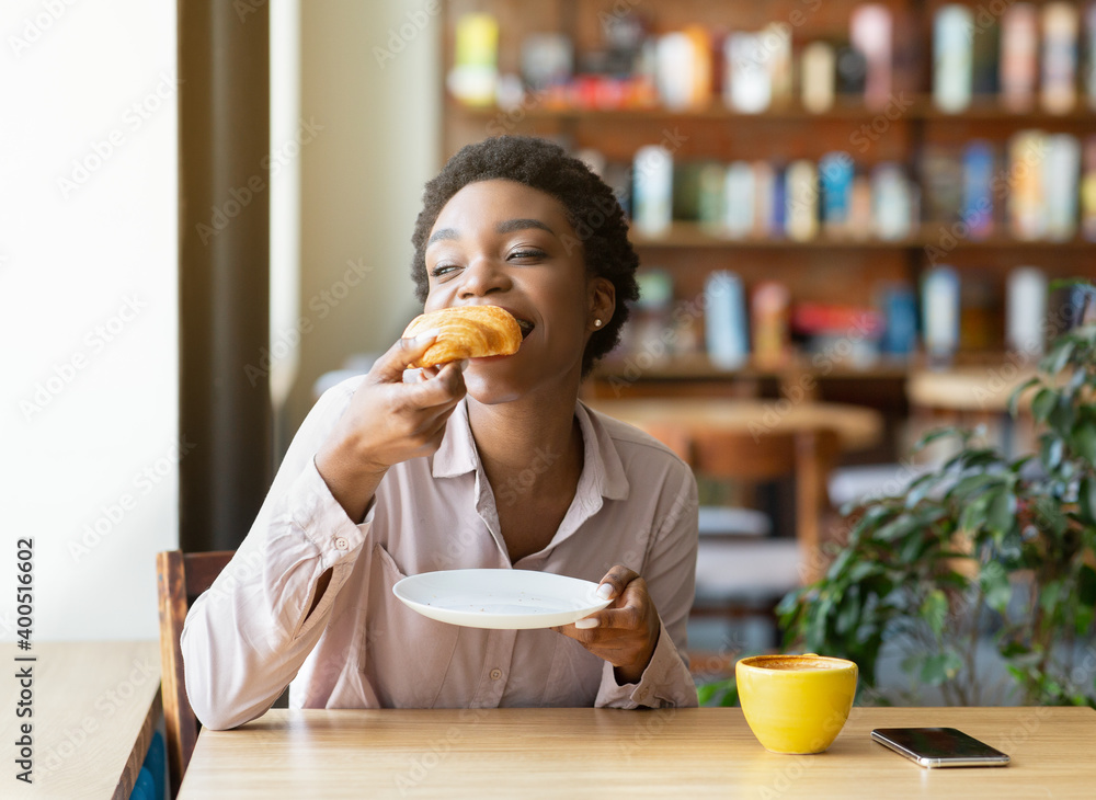 Pretty black woman enjoying breakfast at cafe, eating fresh croissant and drinking aromatic coffee Pretty black woman enjoying breakfast at cafe, eating fresh croissant and drinking aromatic coffee