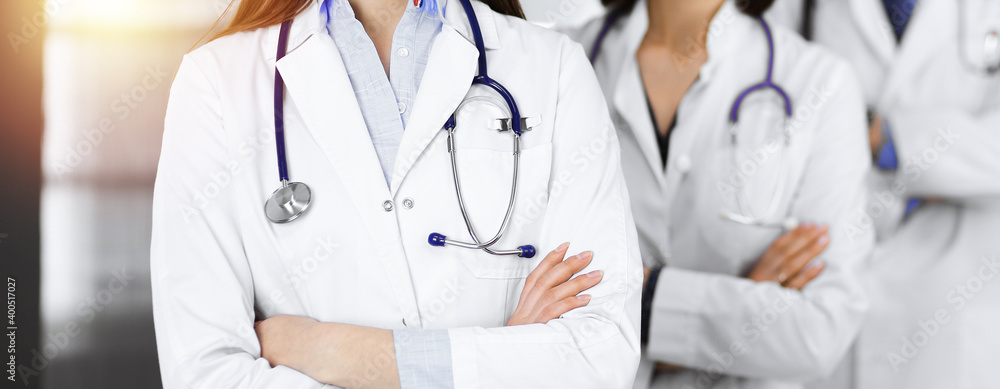 Group of professional doctors is standing as a team with arms crossed in sunny clinic. Medicine concept during Coronavirus pandemic. Covid-2019 Group of professional doctors is standing as a team with arms crossed in sunny clinic. Medicine concept during Coronavirus pandemic. Covid-2019