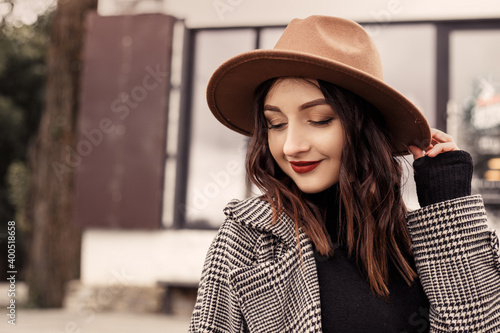 Close up shot charming woman standing outside near street cafe restaurant wear brown hat gray coat poloneck black sweater, looking away. Girl spend time autumn or spring, cold weather fresh air.