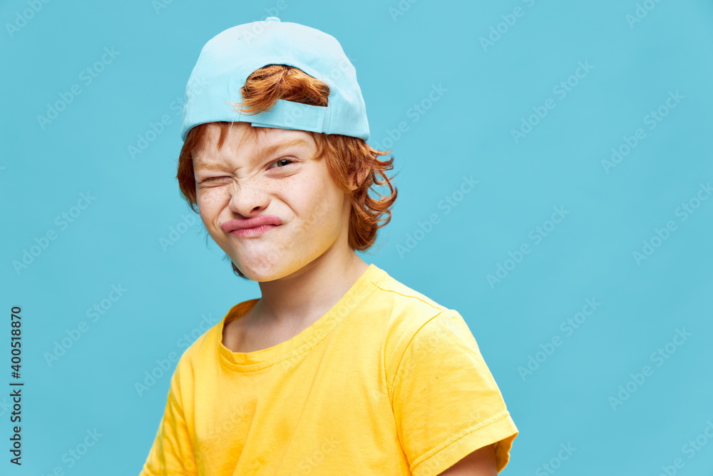 Red-haired boy with a cap on his head grimacing yellow t-shirt 