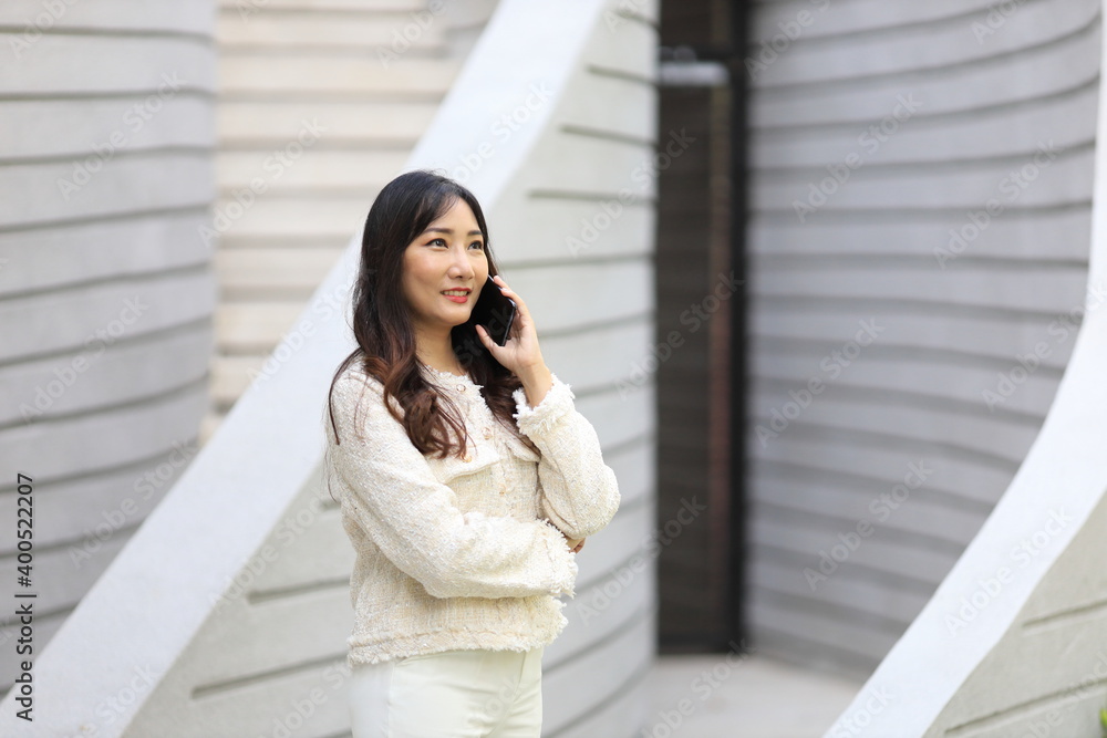 Asian lady using mobile phone while walking along the modern building in urban downtown area for communication and technology concept Asian lady using mobile phone while walking along the modern building in urban downtown area for communication and technology concept