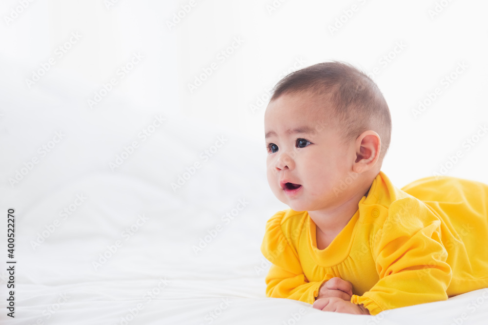 Portrait of beautiful young Asian newborn little baby prone on the bed at home, Happy baby smile wears a yellow shirt relaxing in the room, Family morning at home