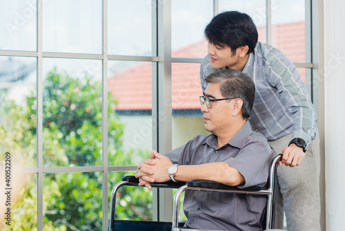 Asian senior disabled businessman in wheelchair discuss interacting together with the team in the office. The old man in a wheelchair and his young son talking to and comforting bound father © sorapop