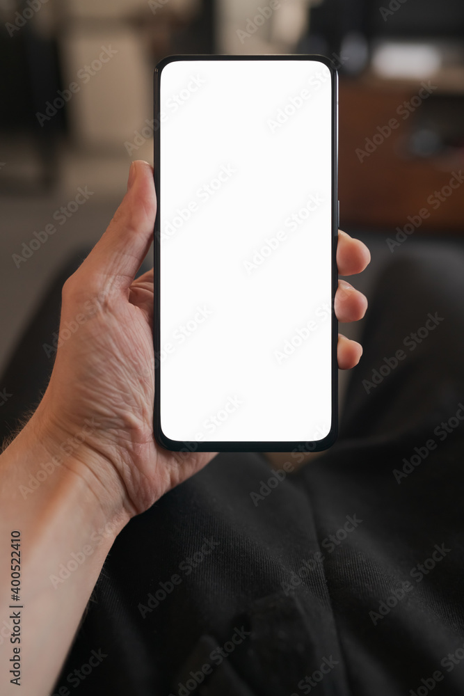 Man hold smartphone with white screen in his hand sitting on a couch in home environment Man hold smartphone with white screen in his hand sitting on a couch in home environment