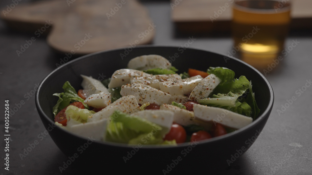 salad with mozzarella and tomatoes in black bowl and apple cider in glass on concrete countertop