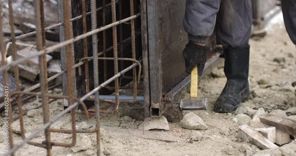 Engineers work with metal constructions while building a house. The worker fixes the form for pouring concrete, aligns metal boards. Filling the foundation of the building Engineers work with metal constructions while building a house. The worker fixes the form for pouring concrete, aligns metal boards. Filling the foundation of the building
