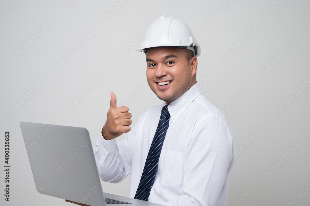 Asian civil engineer operate with laptop to control working in studio. Worker wearing hard hat using laptop computer standing showing thumbs up on isolated white background. Asian civil engineer operate with laptop to control working in studio. Worker wearing hard hat using laptop computer standing showing thumbs up on isolated white background.