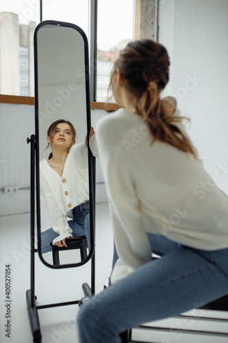 Photo portrait of young woman looking at mirror reflection wearing casual clothes sitting in front of window
