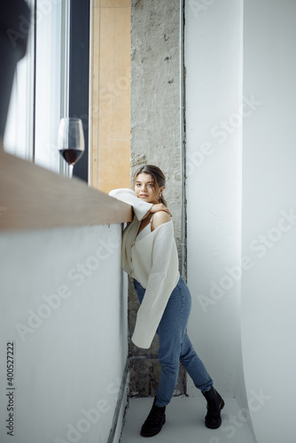 full length body size photo of pretty model wearing blue jeans white warm cardigan posing near glass of red wine indoors