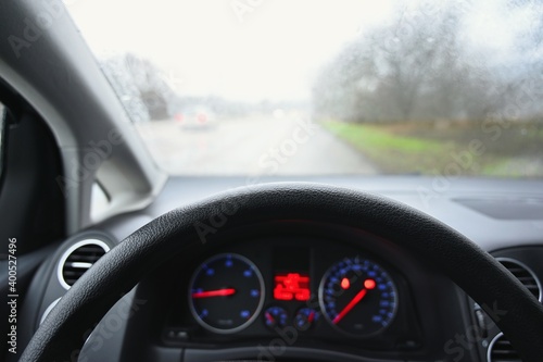 View from the driver - car interior with steering wheel and dashboard. Winter bad rainy weather and dangerous driving on the road.