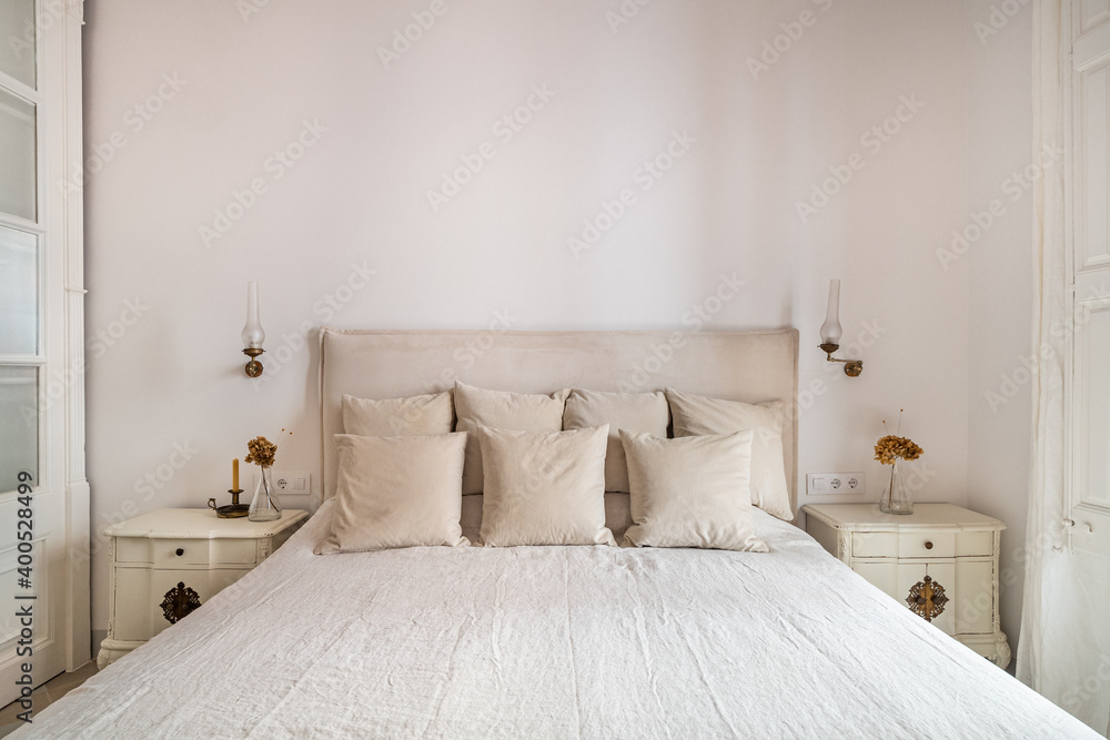 Bright bedroom interior, cozy bed with beige linen, dry flowers on a bedside table Bright bedroom interior, cozy bed with beige linen, dry flowers on a bedside table