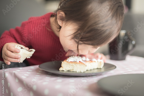 A toddler wearing a red top licks a piece of cake with cream on a plate as she holds another piece on her hand in a house in Edinburgh  Scotland  United Kingdom